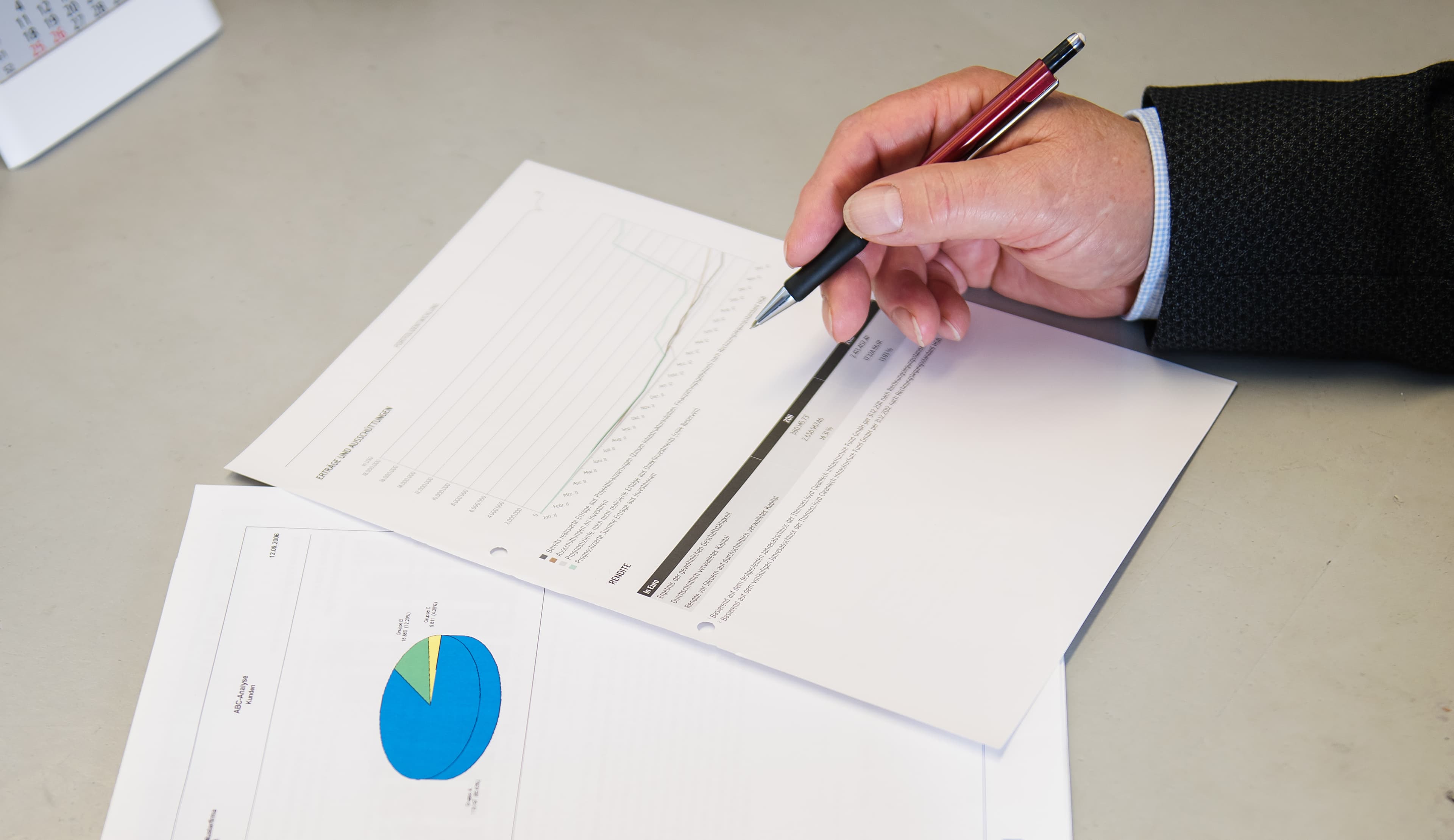 Eine Hand mit rotem Stift prüft Finanzunterlagen und Auswertungen.